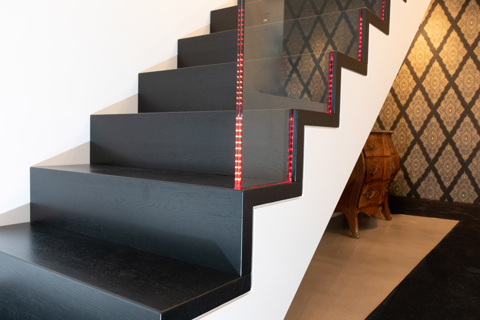 Treppengeländer mit eingenutetem Glas und farbwechselnder LED-Beleuchtung für modernes Ambiente auf schwarzen Stufen für maximalen Kontrast