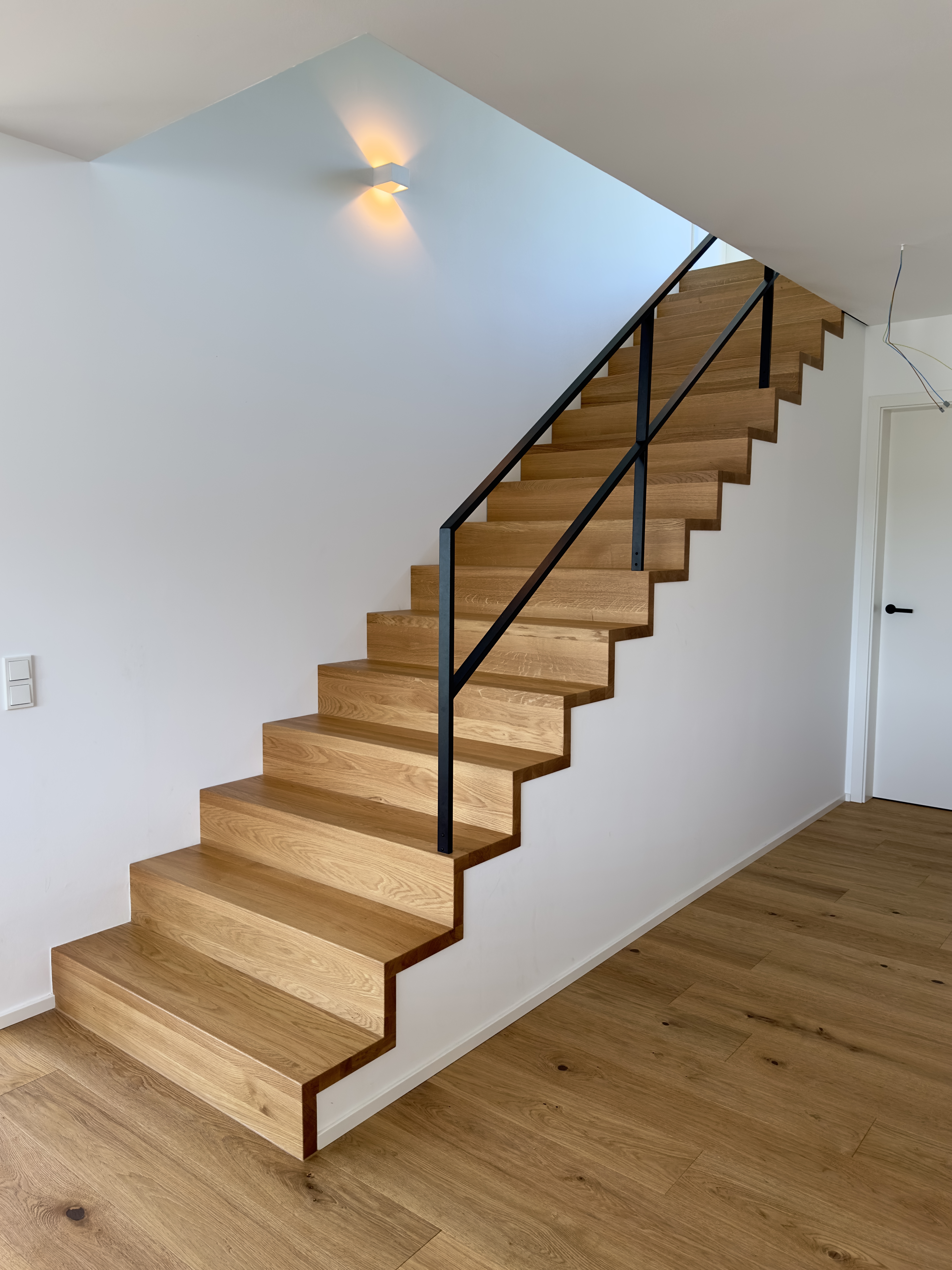 Gerade Treppe mit Winkelstufen und schwarzem Stahlgeländer im offenem Wohnraum